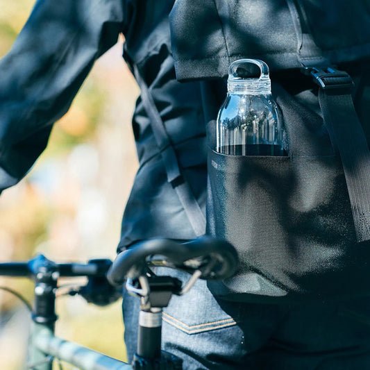 Person holding a water bottle in a bike bag with a blurred natural background